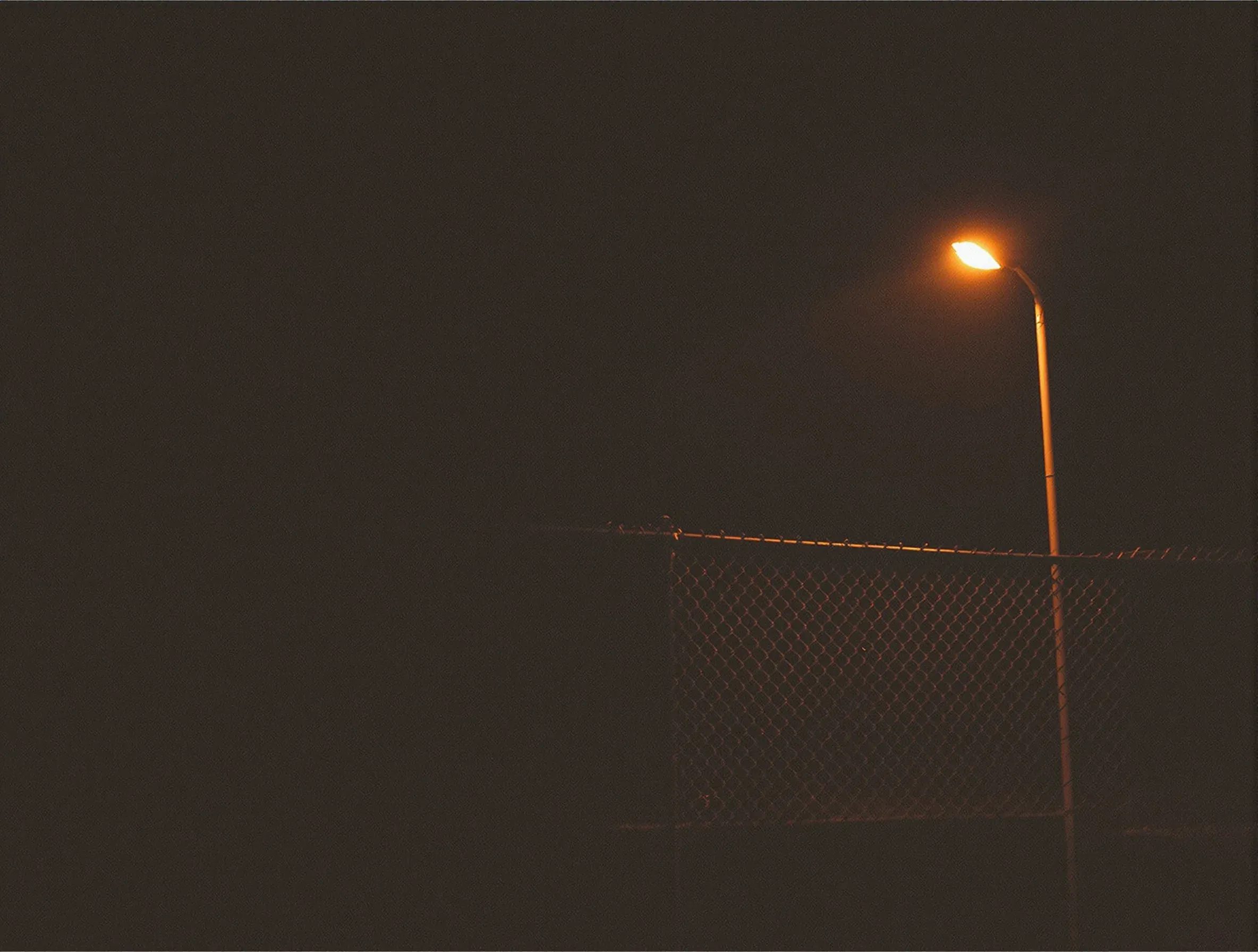 A chain link fence at night lit from one side by a security lamp