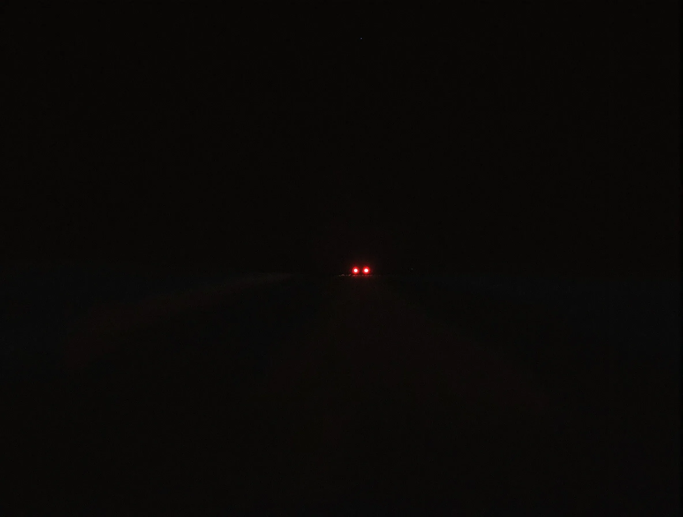 An open desert highway at dusk with red tail lights far in the distance