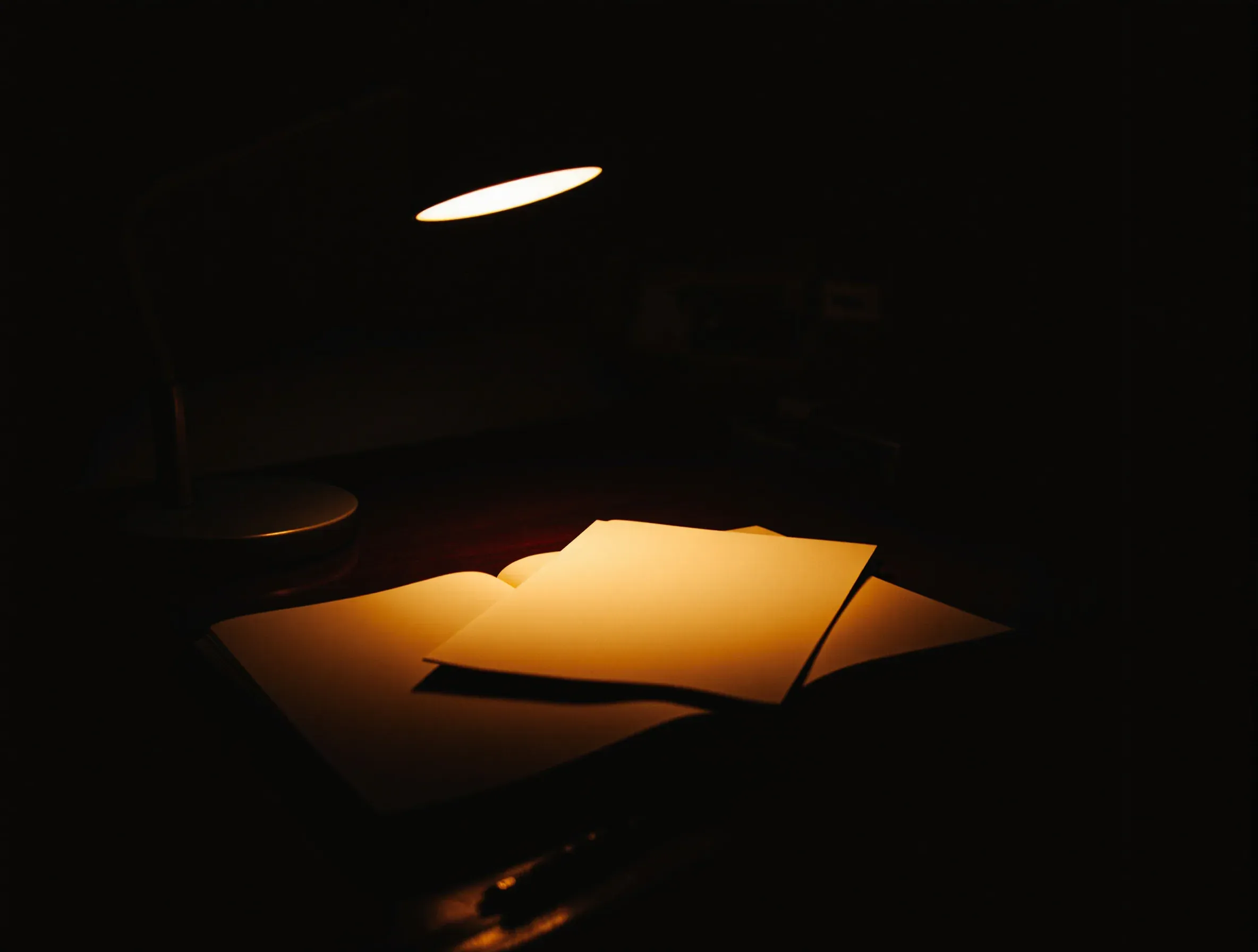 A desk lamp throwing a warm pool of light over an open notepad at night