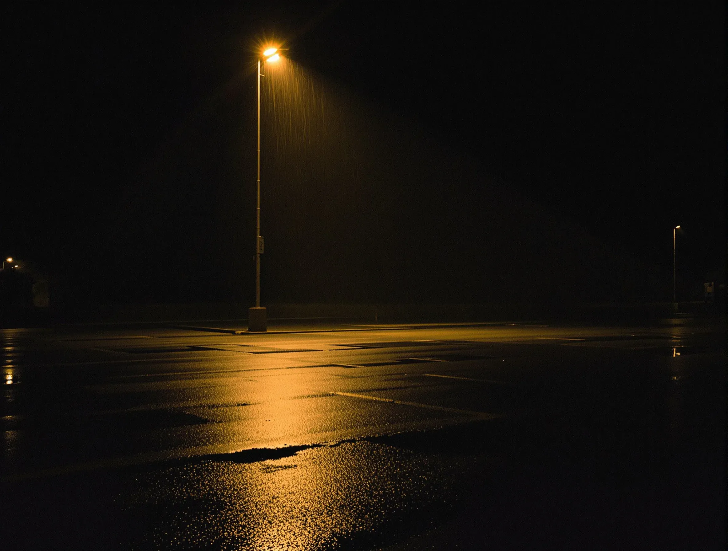 An empty car park after rain with one floodlight reflected across the wet ground
