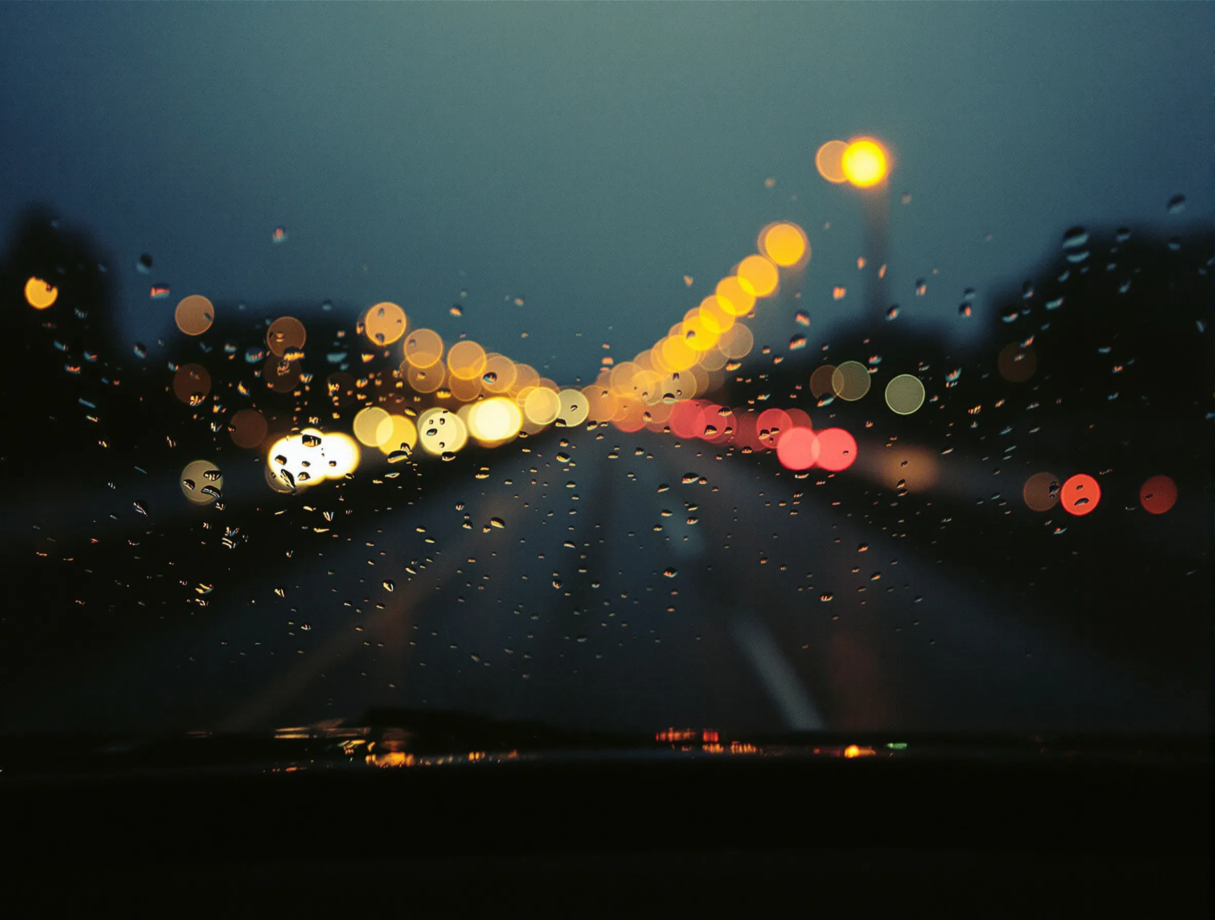 Rain running down a windscreen at night with freeway lights blurred beyond